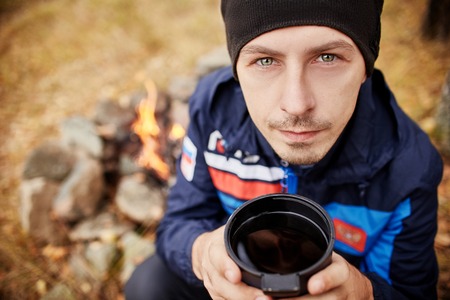 Portrait of a Man with a mug of hot tea in his hands fall in a forest fire. A picnic in the autumn...