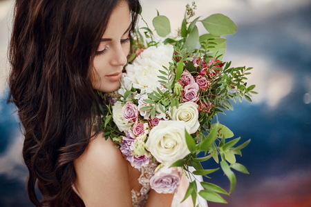 Portrait woman with blue eyes and bouquet of flowers in her hands on nature. Gorgeous hair and perfect skin, beautiful natural makeup. Girl with a bouquet of roses, mysterious dream image womanの写真素材