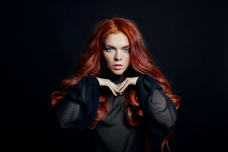 Beautiful woman with red hair on a black background. Portrait of a successful woman, pure skin, natural makeup, skin care face. Contrast portrait of a adult girlの写真素材