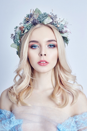 Portrait of a blonde woman with a wreath on her head and a blue delicate light transparent dress. Big blue eyes and beautiful skin. Fabulous mysterious magical portrait of a womanの写真素材
