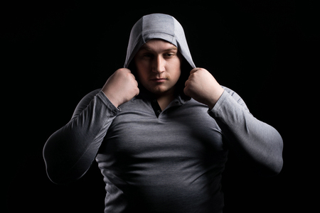 Sports large muscular man in a hood on black background contrasting portrait. Fitness and strength liftingの写真素材