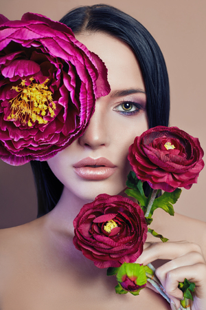 Large peonies near a woman face, art fashion flowers in front of a girl, nature face care, natural cosmetics and professional makeup, beige background. Purity hair eyes and makeup sexy girlsの写真素材