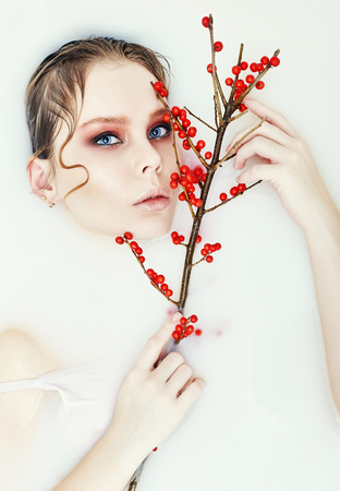 Tree Branch with red berries in hand Woman blonde wet hair bright beautiful art makeup portrait closeup. Perfect facial skin hydration and Spa. Summer skincare fashion. Bathroom water milkの写真素材