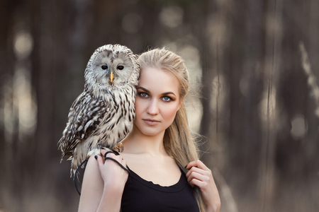 Woman blond in autumn in fur coat with owl on hand first snow. Beautiful girl with long hair in nature, holding an owl. Romantic, delicate look girlsの写真素材