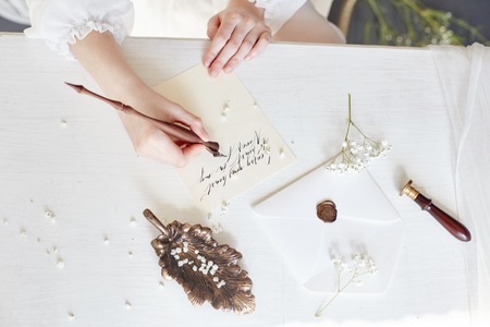 Girl writes a letter to her beloved man, sitting at home at table in a white light dress, purity and...