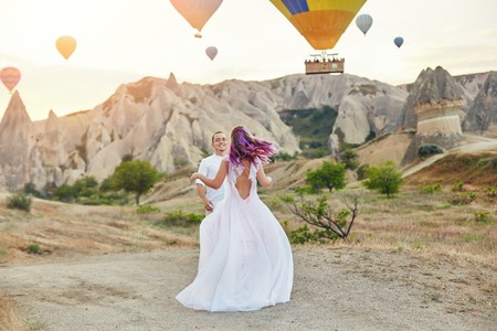 Couple in love stands on background of balloons in Cappadocia. Man and a woman on hill look at a large number of flying balloons. Turkey Cappadocia fairytale scenery of mountains. Wedding on natureの写真素材