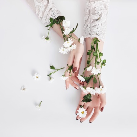Natural beauty hand cosmetics with flower extract, product. Summer Fashion woman hand on the table with flower, skin care. Creative makeup, girl hands lying on the table, white backgroundの写真素材