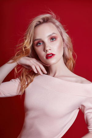 Sexy fashion blonde with bright red makeup on bright red background. Girl in lingerie body with a perfect figure. Professional make-up, skin care, natural cosmetics for face, beautiful eyesの写真素材