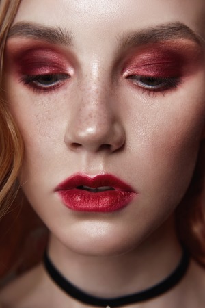 Portrait of a blonde woman with flower petals on her face close-up, bright red makeup and lipstick....