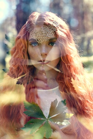 Fabulous portrait of a red-haired girl in nature with double exposure and glare. Beautiful redhead...