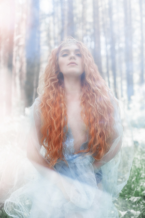 Beautiful redhead woman forest nymph in a blue transparent light dress in the woods spinning in dance. Red hair girls. Art fashion portrait of fairy woman fairy tale in summer forestの写真素材
