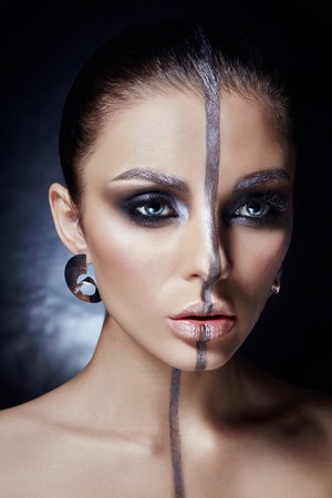 Creative makeup on woman face, beautiful big eyes. Fashion Perfect makeup, silver color band on the girl face, silver eyebrows and black brunette hair. Portrait of a woman on a dark backgroundの写真素材