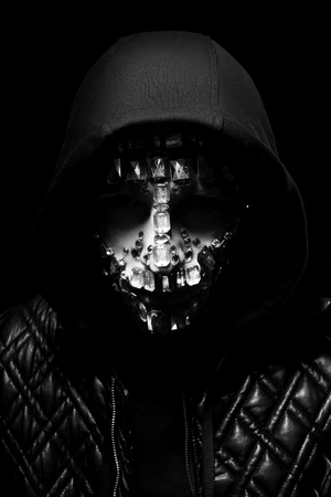 Art portrait of a hooded man with big rhinestones on his face. Mysterious mystical appearance of a man. Big crystals glisten in the dark on the guy face. Blurred out of focusの写真素材