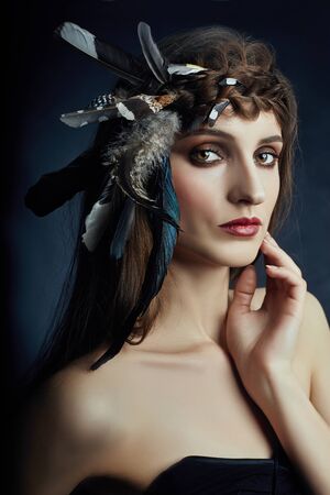 Indian woman with feathers in her hair, portrait of American Indian girl beauty on dark background in smoke. Beautiful face with clean skin, contrast makeupの写真素材