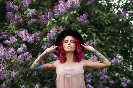 Spring beauty portrait of a beautiful girl with red hair in the branches of a blooming lilac. Lilac flowers in the hands and hair of a woman. Natural makeupの写真素材