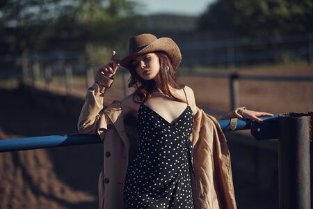 Girl in a cowboy hat resting in the village near the stables, portrait of a woman in the sun, rustic style. Portrait of a sexy brunette in nature. Perfect makeup, natural cosmeticsの写真素材