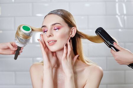 Girl is doing her hair in a beauty salon, hair styling and combing. Woman with bright shiny creative makeup in beauty salon, hair careの写真素材