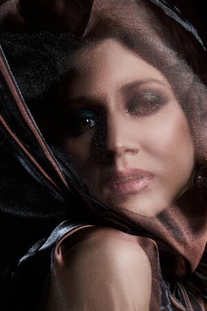 Portrait of a brunette woman through a transparent dark fabric. Beauty and makeup girl. There is no...