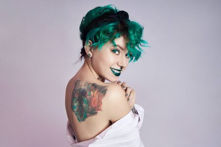 Woman with creative green coloring hair and makeup, toxic strands of hair. Bright color curly hair on the girl head, professional makeup. Woman with tattooの写真素材