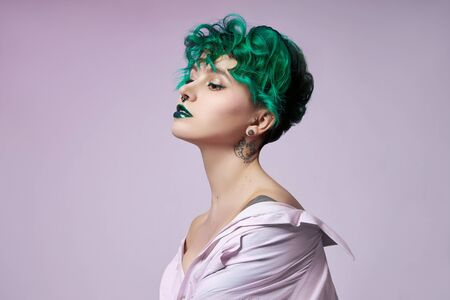 Woman with creative green coloring hair and makeup, toxic strands of hair. Bright color curly hair on the girl head, professional makeup. Woman with tattooの写真素材