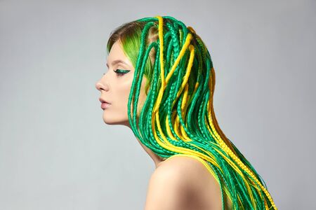 Portrait of a woman with creatively colored hair in green and yellow color. Colorful bright dreadlocks, beautiful modern makeupの写真素材