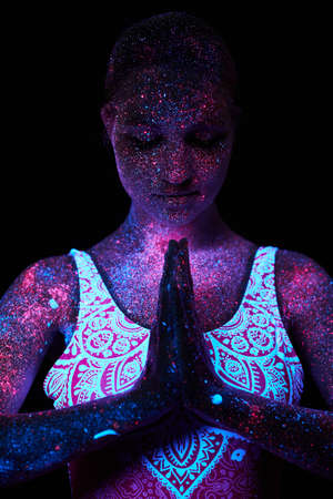 Woman does yoga, hand movement, body warm-up. Art girl cosmos in ultraviolet light. Entire body is covered with colored droplets. Astral yoga. Noise, out of focusの写真素材