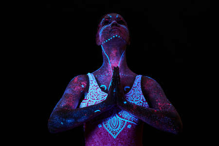 Art girl cosmos in ultraviolet light. Woman does yoga, body warm-up. Entire body is covered with colored droplets. Astral yoga. Noise, out of focusの写真素材