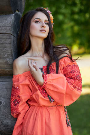 Beautiful Slavic woman in an orange ethnic dress and a wreath of flowers on her head. Beautiful...
