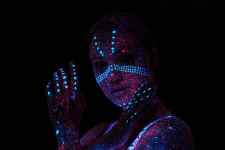 Art woman cosmos in ultraviolet light. Entire body is covered with colored droplets. Girl posing in the dark. Noise, out of focusの写真素材