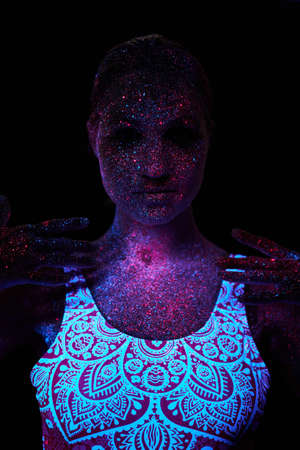 Art woman cosmos in ultraviolet light. Entire body is covered with colored droplets. Girl posing in the dark. Noise, out of focusの写真素材