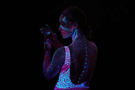 Art woman cosmos in ultraviolet light. Entire body is covered with colored droplets. Girl posing in...