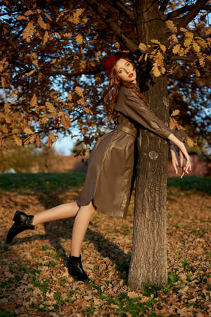 Autumn portrait of a woman in a hat beret and raincoat near a tree in autumn yellow foliageの写真素材