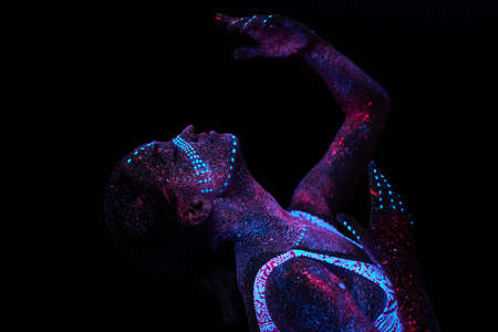 Art woman cosmos in ultraviolet light. Entire body is covered with colored droplets. Girl posing in the dark. Noise, out of focusの写真素材