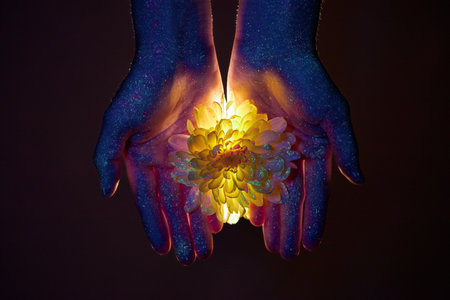 Beauty hands of a woman in ultraviolet light with flowers in the palms. Cosmetics for hand skin careの写真素材