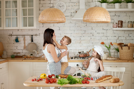 Family prepares lunch in the kitchen. Mom teaches her daughter and son to prepare a Salad of fresh vegetables. Healthy natural food, vitamins for childrenの写真素材