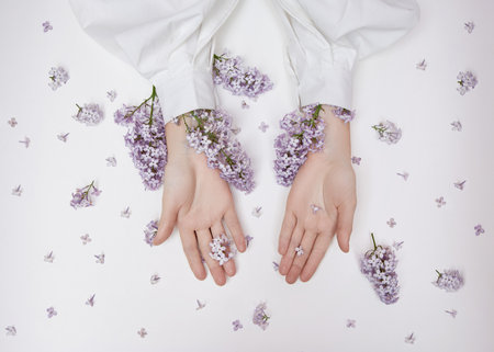 Natural woman cosmetics for hands made of lilac flowers and petals. Moisturize and soften the skin of the hands. Lilac flowers protrude from the sleeves of the armの写真素材