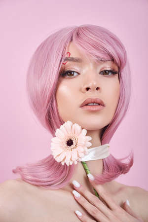 Beautiful woman with dyed pink hair guessing at flower in hand at table with candles. Pink beauty hair on head of woman fortune teller. Beauty Girl with flower in her handの写真素材