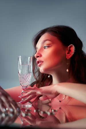 Woman holds a glass glass in her beauty hand. Rings and jewelry on table, luxurious life. Alcoholismの写真素材