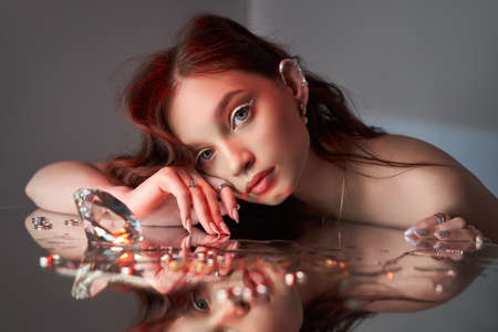 Woman holds a glass glass in her beauty hand. Rings and jewelry on table, luxurious life. Alcoholismの写真素材