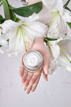 Beauty jar cream hand cosmetic woman with lily flowers lie on table, jar cream product in hand woman...