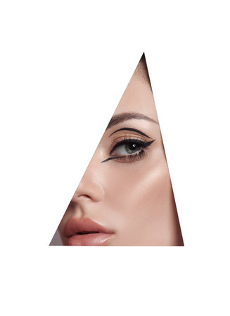 Beauty makeup women, eye brows eyelashes and lips in a triangular hole paper white background. Professional beauty makeup, place for text, copy spaceの写真素材