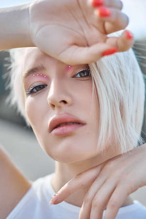 Perfect red nail manicure blonde woman short hair. A woman poses in summer in nature on a sunny day