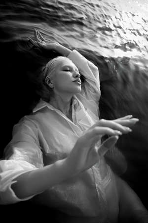 Beautiful blonde woman short hair lies in water on sea shore, pond. Art portrait of a relaxing woman in the water on shoreの写真素材