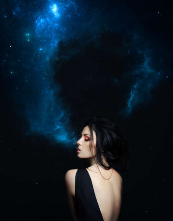 Brunette woman Smoking cosmos galaxy on dark star background in black dress. Art Fashion girl