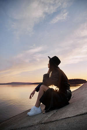 Beautiful woman in light red dress stands in water of lake sea at sunset. Reflection of the girl and...