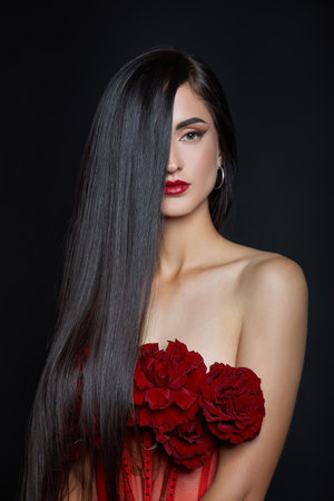 Beautiful brunette woman with a bouquet of red rose flowers in red corset. Long hair, nude slim body art portraitの写真素材