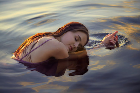 Beautiful young woman in lake water in summer dress at sunset. Portrait of a romantic wet girl at...
