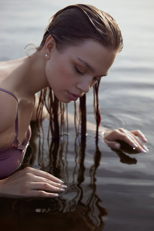 Beautiful romantic woman sitting near a pond lake. Wet woman in her underwear in the rays of the sun at sunset. natural beauty long hairの写真素材