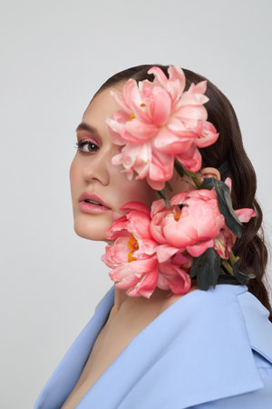 Fashion woman in blue suit with pink flowers, beauty face portrait. Art studio portrait of a young woman on a white background, pink makeupの写真素材