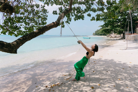 Woman enjoys a peaceful swing on a rope tied to a tree, against the backdrop of a tranquil beach and...